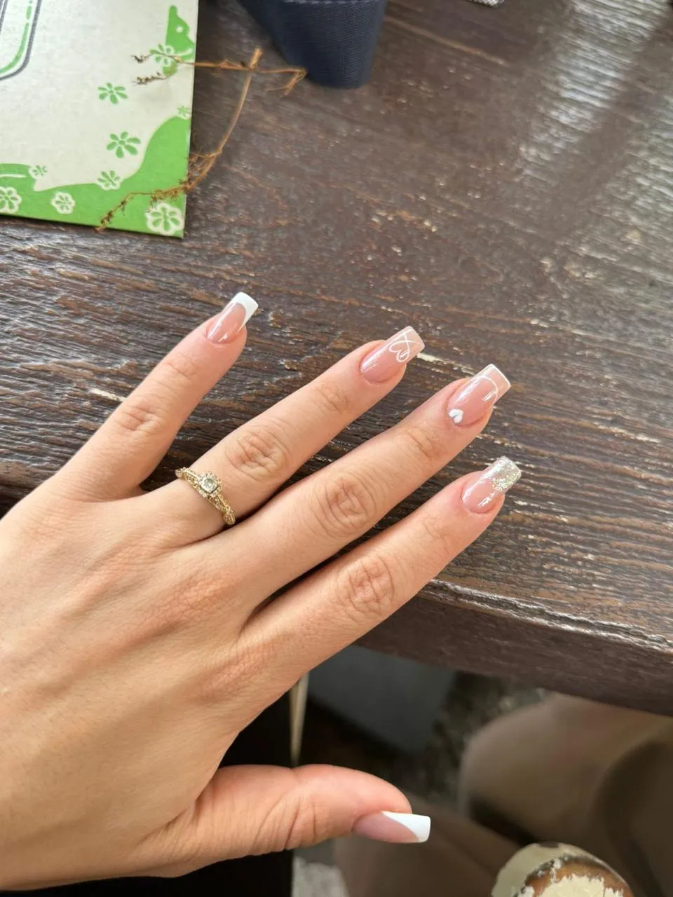 Uñas acrílicas largas con puntas francesas sobre una mesa de madera